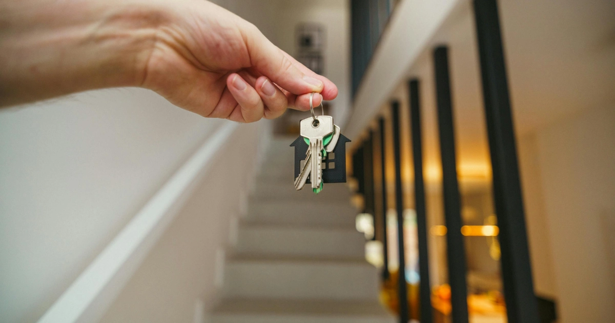 Mano sosteniendo las llaves de una casa nueva con un llavero en forma de hogar, simbolizando la entrega de llaves al comprar una segunda vivienda en Espa?a.