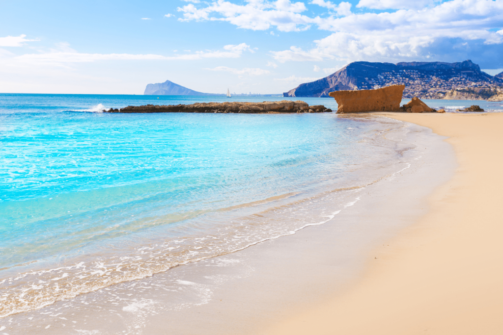 Beaches of the Costa Blanca where you can see a blue sea, the characteristic sand and a rocky breakwater.