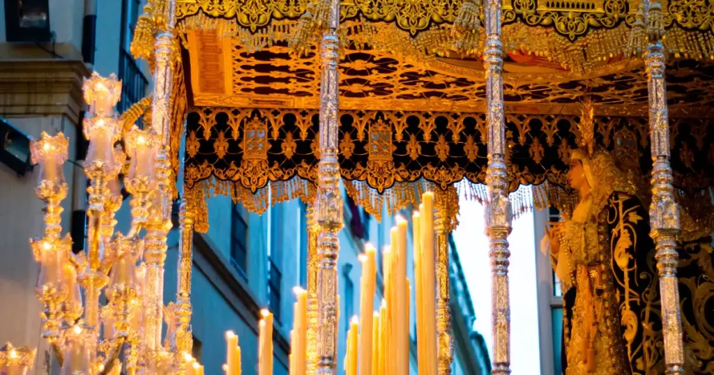 Detalle de un trono de Semana Santa en Málaga con velas encendidas y palio bordado en oro
