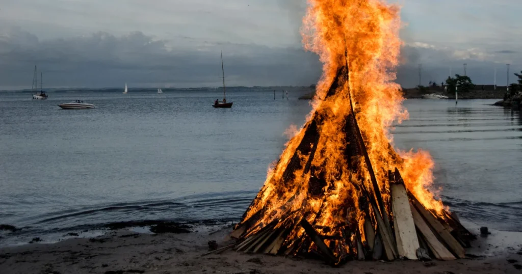 Gran hoguera de San Juan ardiendo en una playa de Málaga al atardecer con barcos al fondo