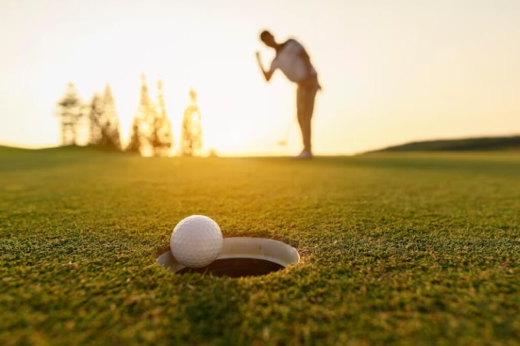Afbeelding van golfer die de golfbal in de hole legt met een zonsondergang.