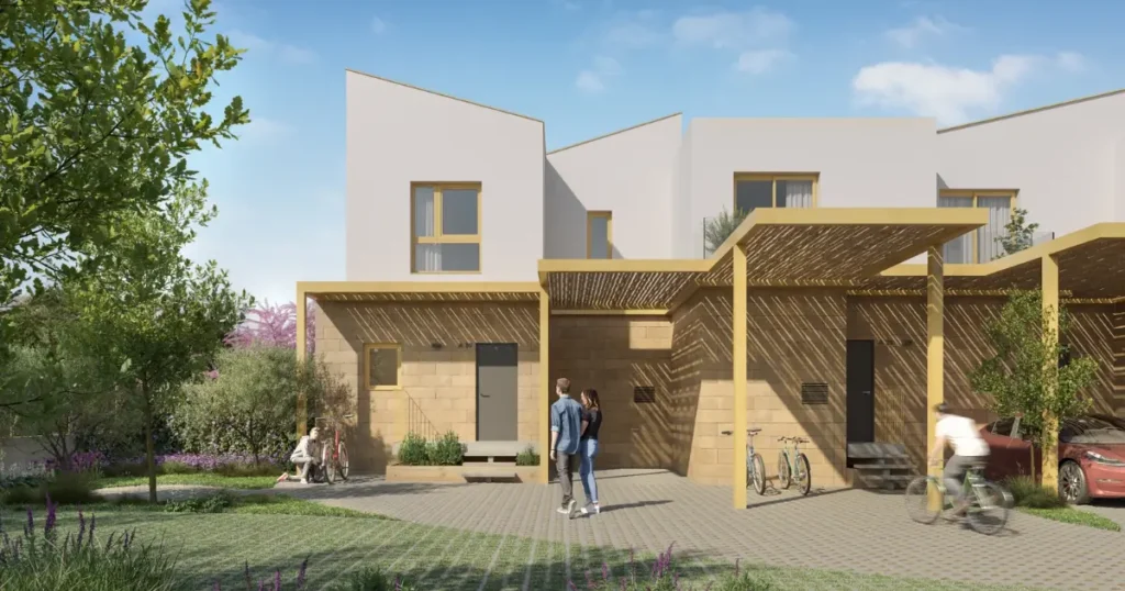 Rendering architektoniczny nowoczesnych dwupi?trowych domów z jasnymi i bia?ymi kamiennymi fasadami, spadzistymi dachami i drewnianymi pergolami. Na zewn?trz kilka os?b spaceruje i je?dzi na rowerze po wybrukowanej ?cie?ce otoczonej zieleni? pod czystym niebem.
